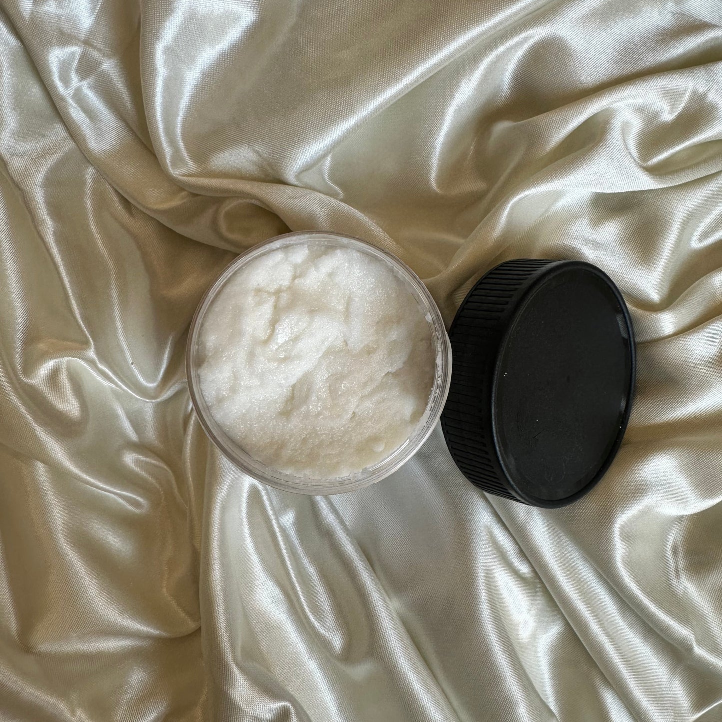 Jar of white cream with a black lid on a white satin surface